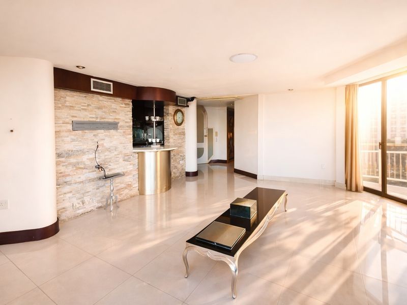 Spacious living area featuring a stone accent wall, integrated bar counter, polished tile flooring, and abundant natural light through large sliding glass doors.