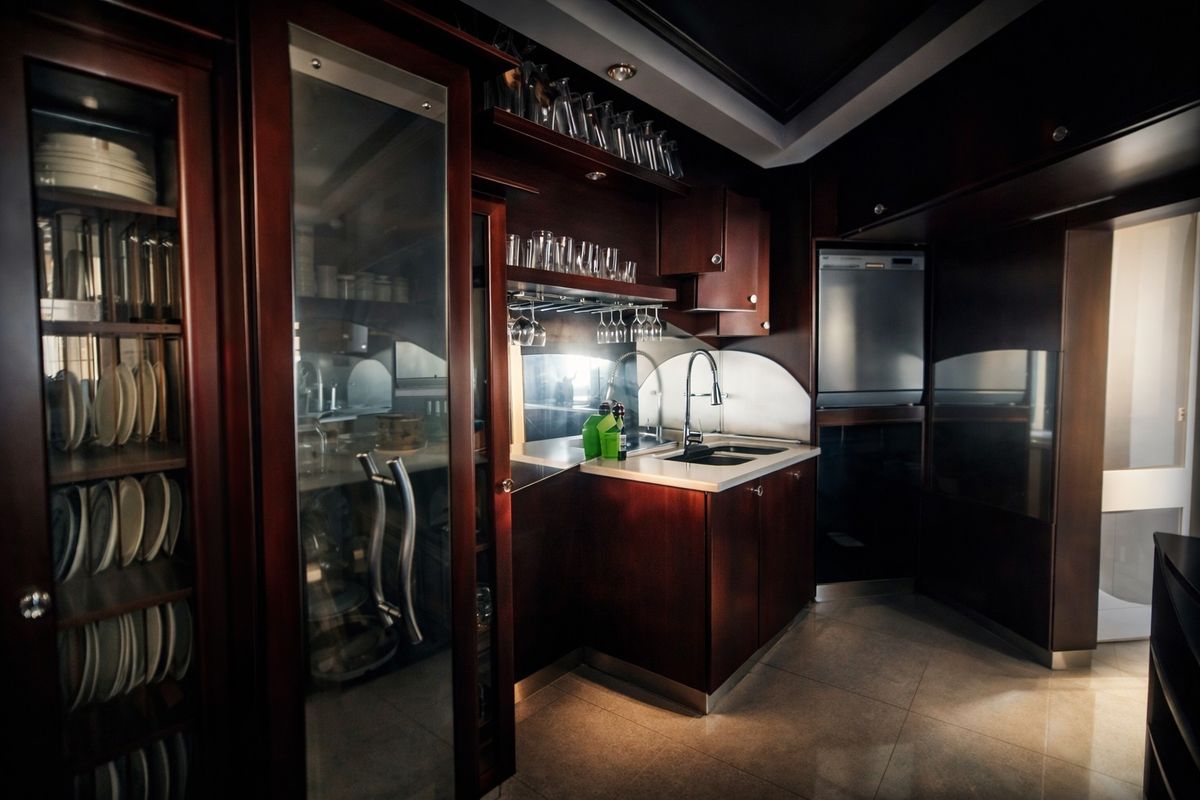 A sophisticated kitchen featuring dark wood cabinetry, glass-fronted display units, stone countertops, and integrated appliances with elegant under-cabinet lighting.