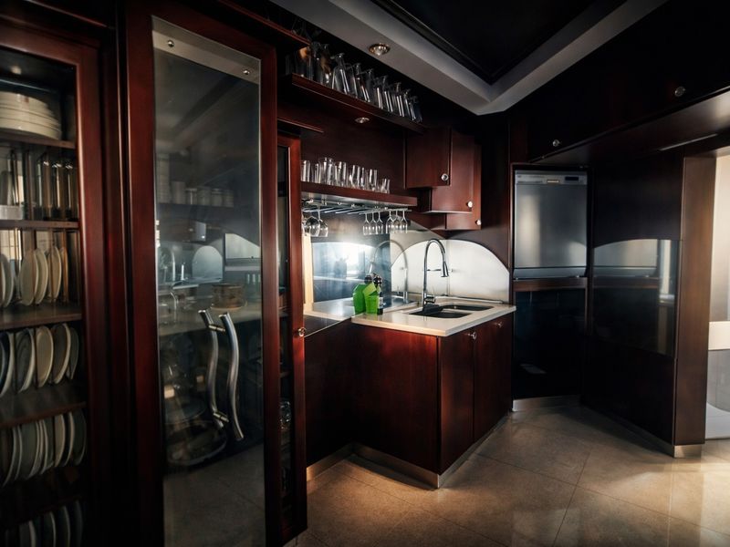 A sophisticated kitchen featuring dark wood cabinetry, glass-fronted display units, stone countertops, and integrated appliances with elegant under-cabinet lighting.