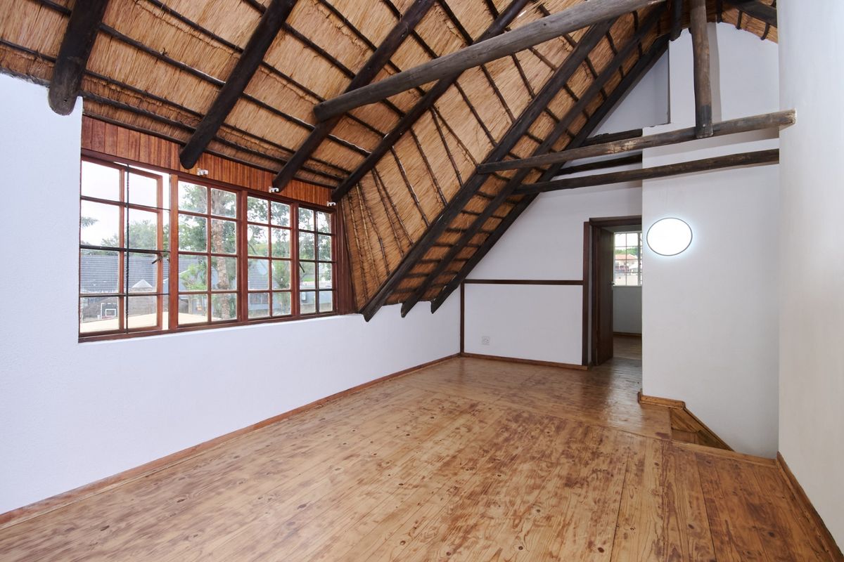 Spacious attic-style bedroom featuring exposed timber rafters, a traditional thatched roof, and warm timber flooring with large windows providing natural light.