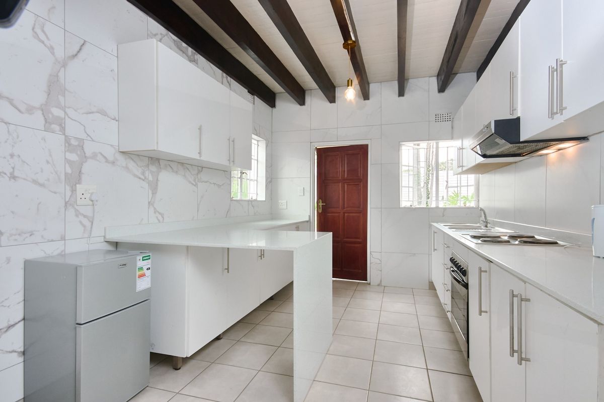 Modern kitchen featuring white cabinetry, stone countertops, marble-look wall tiles, and exposed timber ceiling beams, offering a clean and functional workspace.