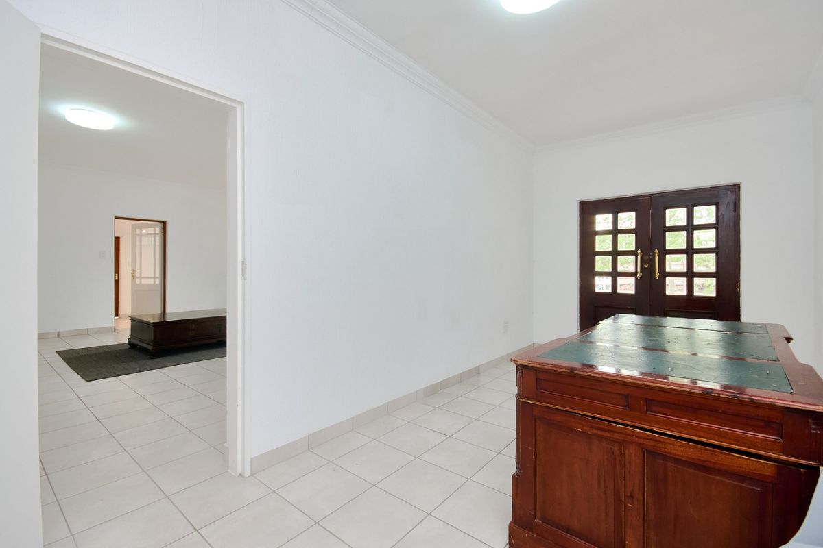 A bright living area featuring neutral tiled flooring, classic ceiling cornicing, and double wooden doors leading to the exterior.