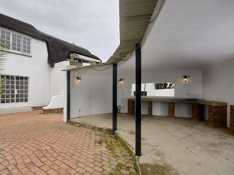 Covered outdoor patio area featuring a built-in brick counter, paved flooring, and direct access to the main residence with a thatched roof.