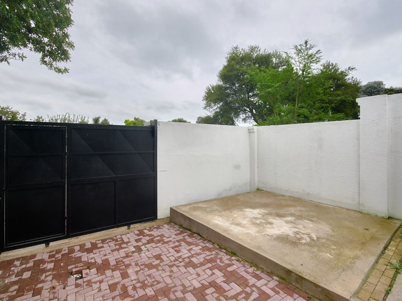A private rear courtyard area featuring a paved surface, a raised concrete platform, and a secure metal gate set within a perimeter wall.