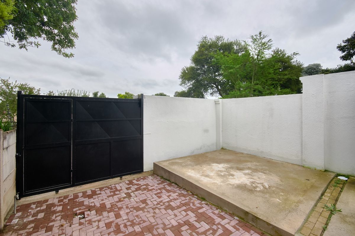 A private rear courtyard area featuring a paved surface, a raised concrete platform, and a secure metal gate set within a perimeter wall.