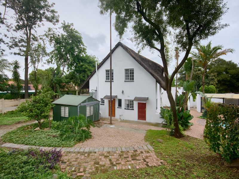 Rear view of a two-story house with a thatched roof, featuring a paved patio area and a detached metal garden shed in the backyard.