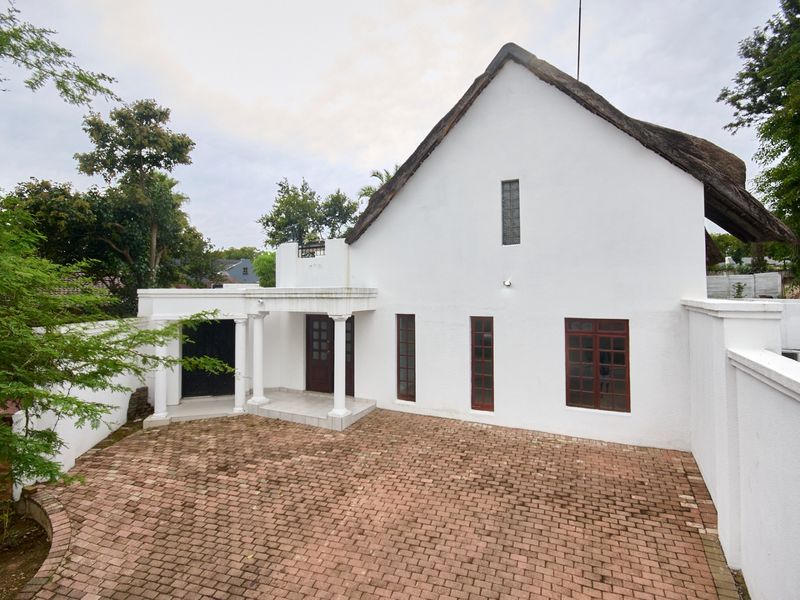 Front exterior view of a house featuring a thatched roof, brick paved driveway, and a covered entrance porch with classical columns.