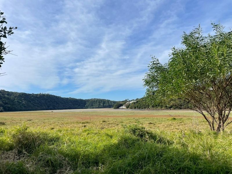 A scenic view of an open grassy landscape with surrounding hills and natural vegetation, showcasing the property's natural surroundings.