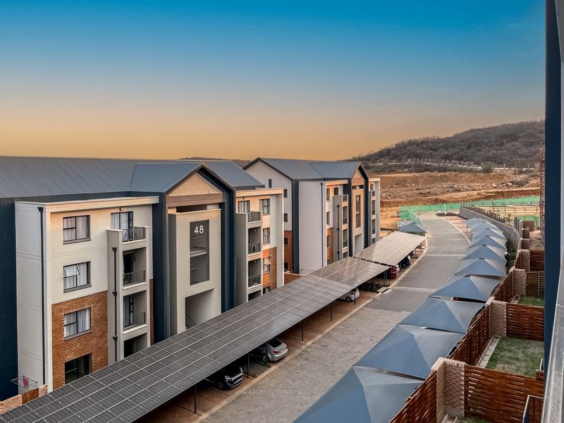 Elevated view of a modern apartment complex featuring brick and render facades, private balconies, and extensive solar-covered parking bays.