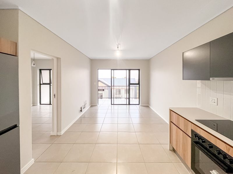 An open-plan living and kitchen area featuring modern cabinetry, built-in appliances, tiled flooring, and a sliding door leading to an outdoor balcony.