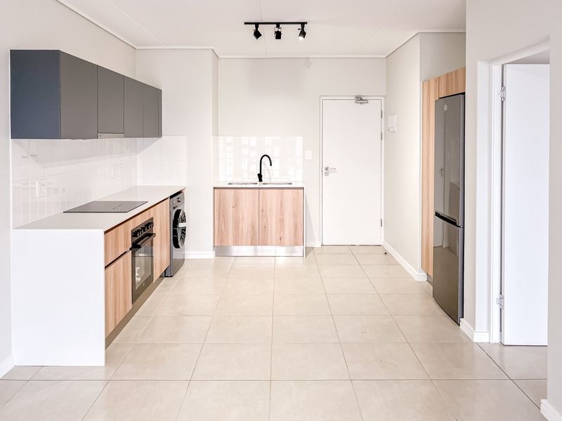 Modern kitchen featuring two-tone cabinetry, integrated electric hob and oven, tiled splashback, and neutral floor tiles in an open-plan layout.