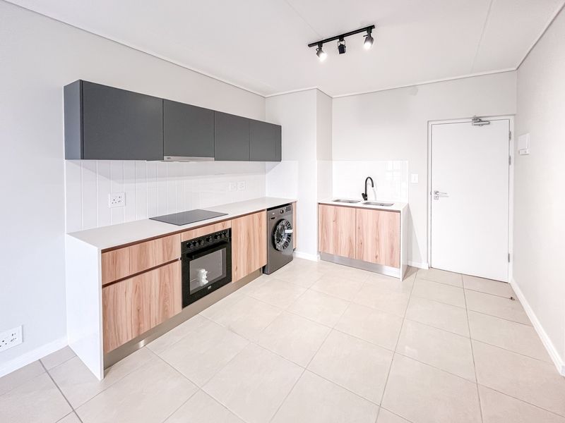 Modern kitchen featuring wood-grain and charcoal cabinetry, integrated oven and hob, tiled backsplash, and neutral floor tiles in an open-plan layout.
