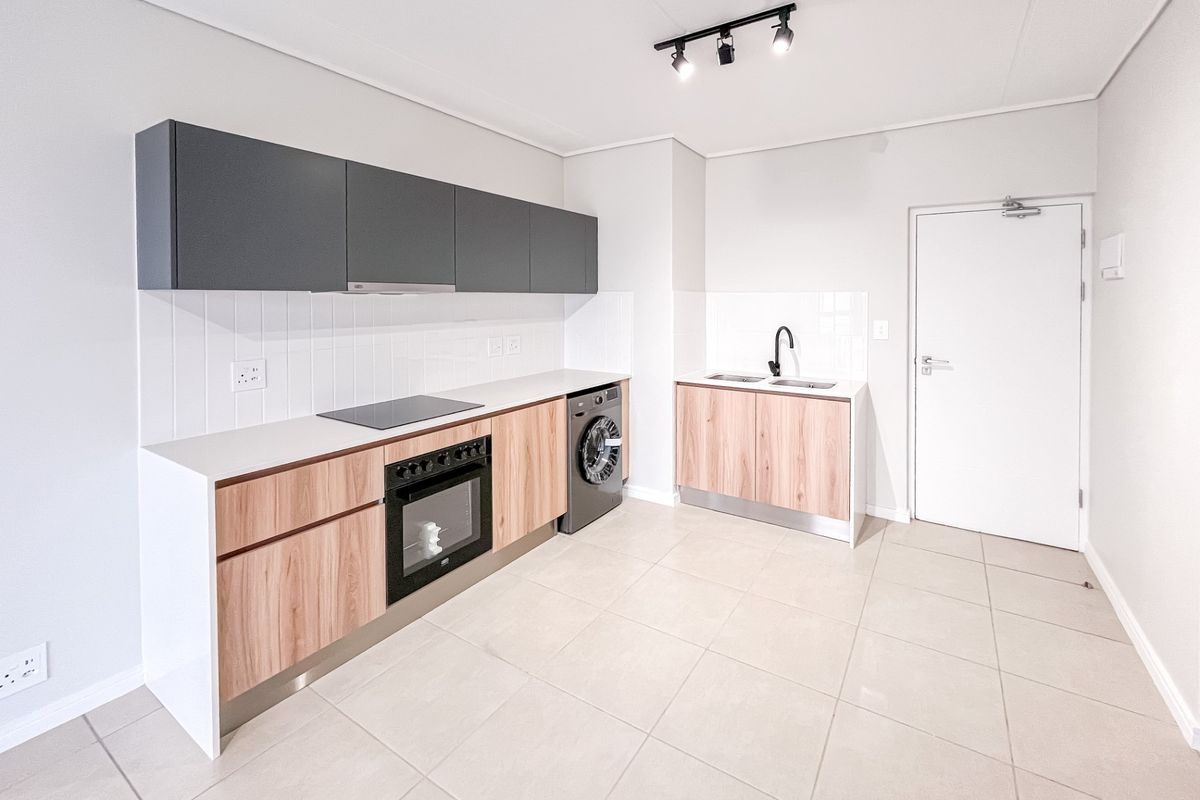Modern kitchen featuring wood-grain and charcoal cabinetry, integrated oven and hob, tiled backsplash, and neutral floor tiles in an open-plan layout.