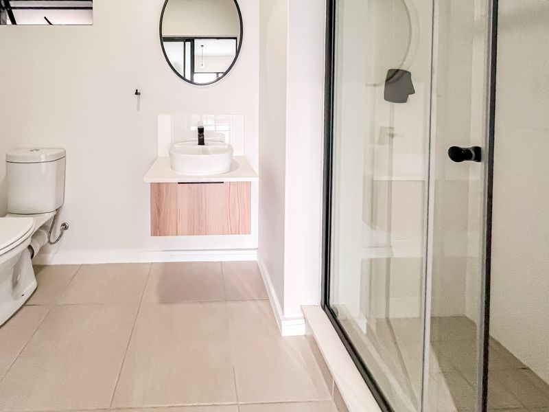 Modern bathroom featuring a wall-mounted vanity with a vessel sink, black fixtures, a toilet, and a glass-enclosed shower with neutral floor tiling.