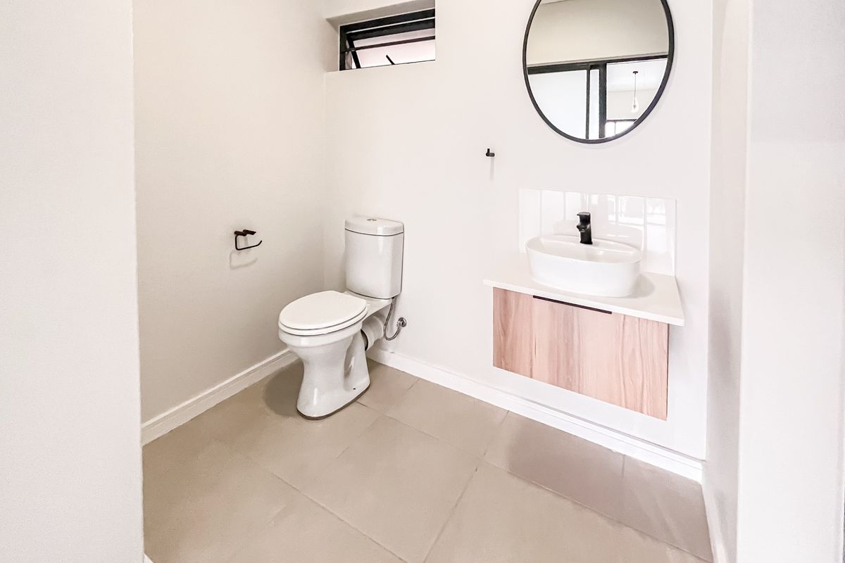 A modern, minimalist guest bathroom featuring a wall-mounted vanity with a vessel sink, black fixtures, and neutral floor tiling.