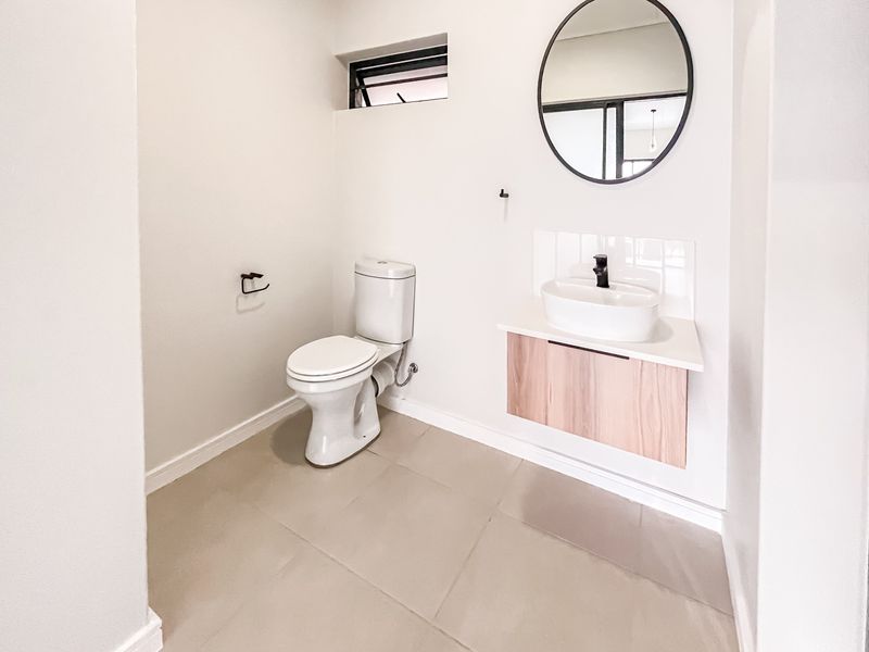A modern, minimalist guest bathroom featuring a wall-mounted vanity with a vessel sink, black fixtures, and neutral floor tiling.