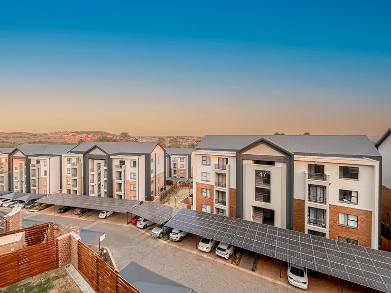 Aerial view of a modern apartment complex featuring multi-story buildings, paved driveways, and extensive solar panel carports.