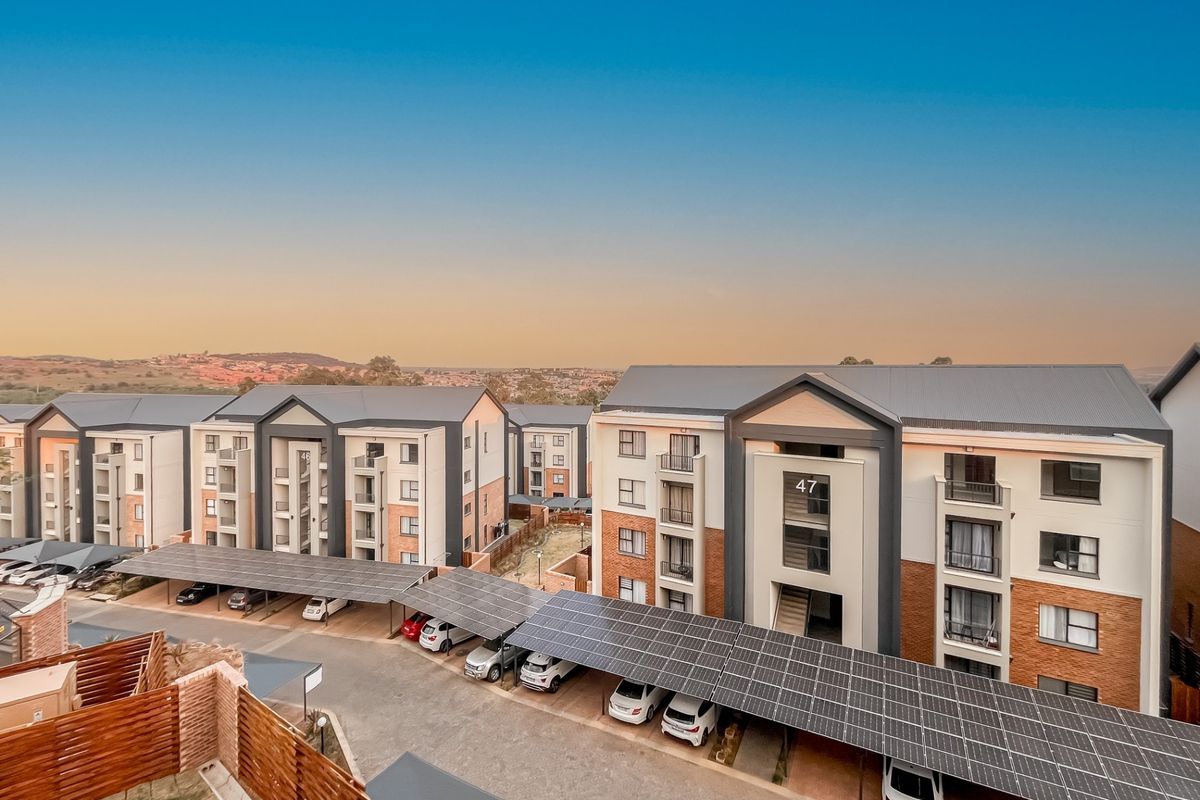 Aerial view of a modern apartment complex featuring multi-story buildings, paved driveways, and extensive solar panel carports.