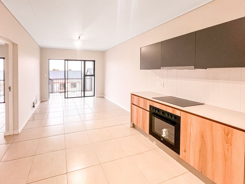 Modern open-plan living area featuring a sleek kitchen with built-in oven, hob, and extractor, leading to a balcony through sliding glass doors.