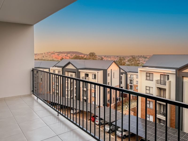 A clean, modern balcony featuring tiled flooring and a secure metal balustrade, offering an elevated view of the surrounding apartment complex and landscape.