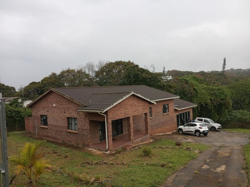 A single-story brick house with a tiled roof, featuring a covered patio entrance and a paved driveway set in a landscaped garden.