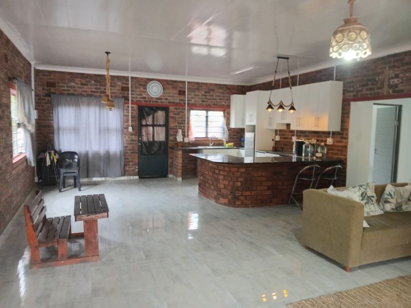 Spacious open-plan living and kitchen area featuring exposed brick walls, a central kitchen island, and tiled flooring throughout.