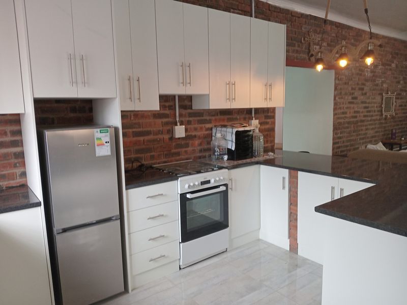 Modern kitchen featuring white cabinetry, granite countertops, built-in oven, gas hob, and a distinctive exposed brick feature wall.