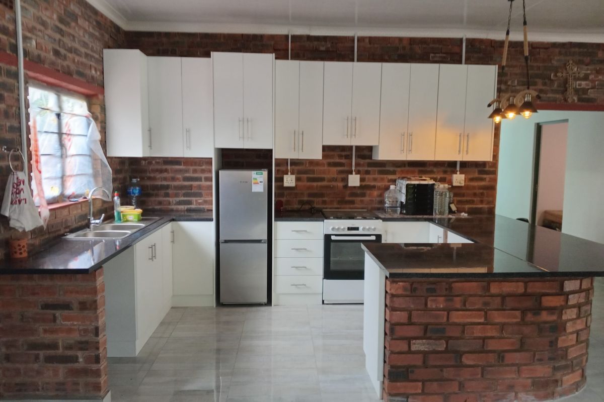 A functional kitchen featuring exposed brick walls, white cabinetry, granite countertops, a breakfast bar, and built-in cooking appliances.