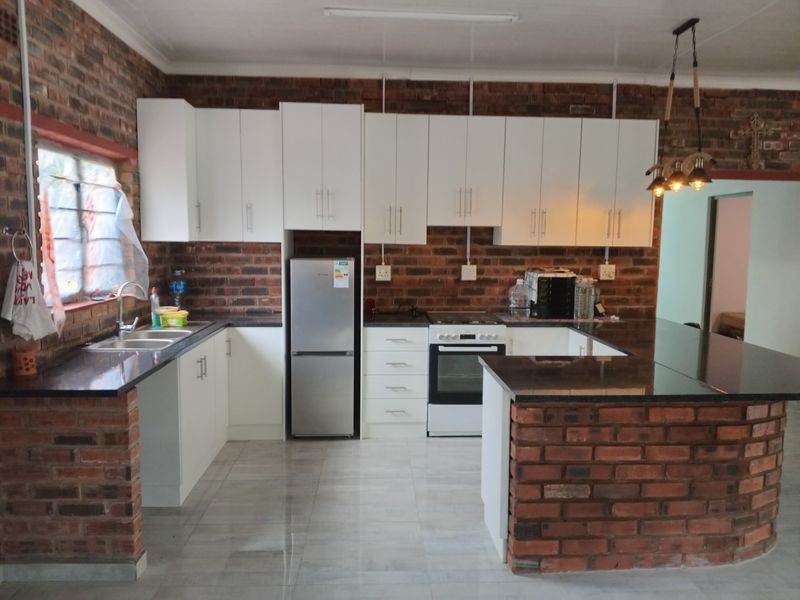 A functional kitchen featuring exposed brick walls, white cabinetry, granite countertops, a breakfast bar, and built-in cooking appliances.