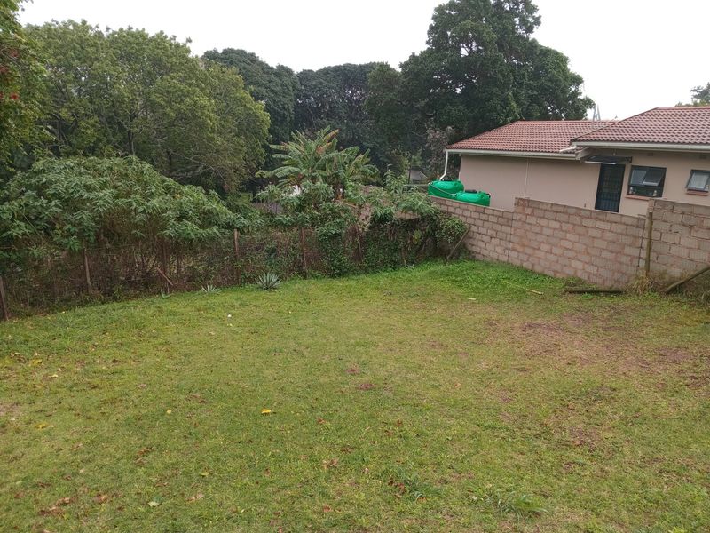 A spacious backyard featuring a lawn, concrete block boundary wall, and water storage tanks, offering potential for landscaping and outdoor development.