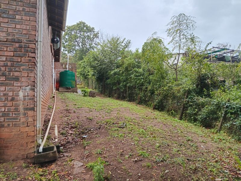 Rear exterior view of the property featuring a brick facade, a rainwater collection tank, and a sloped garden area with perimeter fencing.