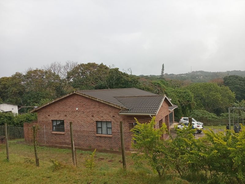 A view of the rear brick exterior of the house featuring a tiled roof and security bars on the windows, set in a natural landscape.
