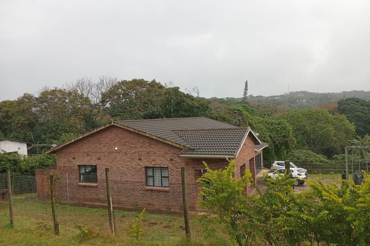 A view of the rear brick exterior of the house featuring a tiled roof and security bars on the windows, set in a natural landscape.