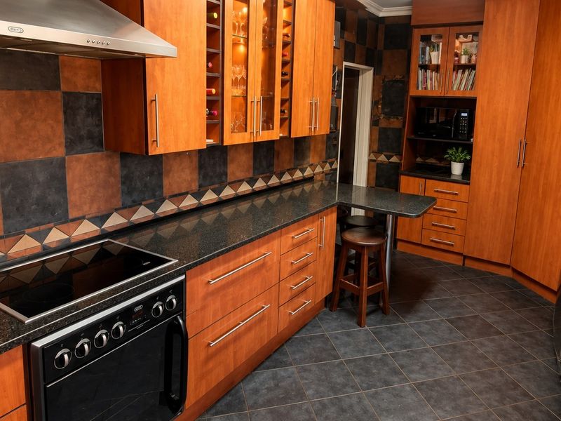 A functional kitchen featuring warm-toned wooden cabinetry, dark granite countertops, a built-in electric stove with extractor fan, and a tiled backsplash.