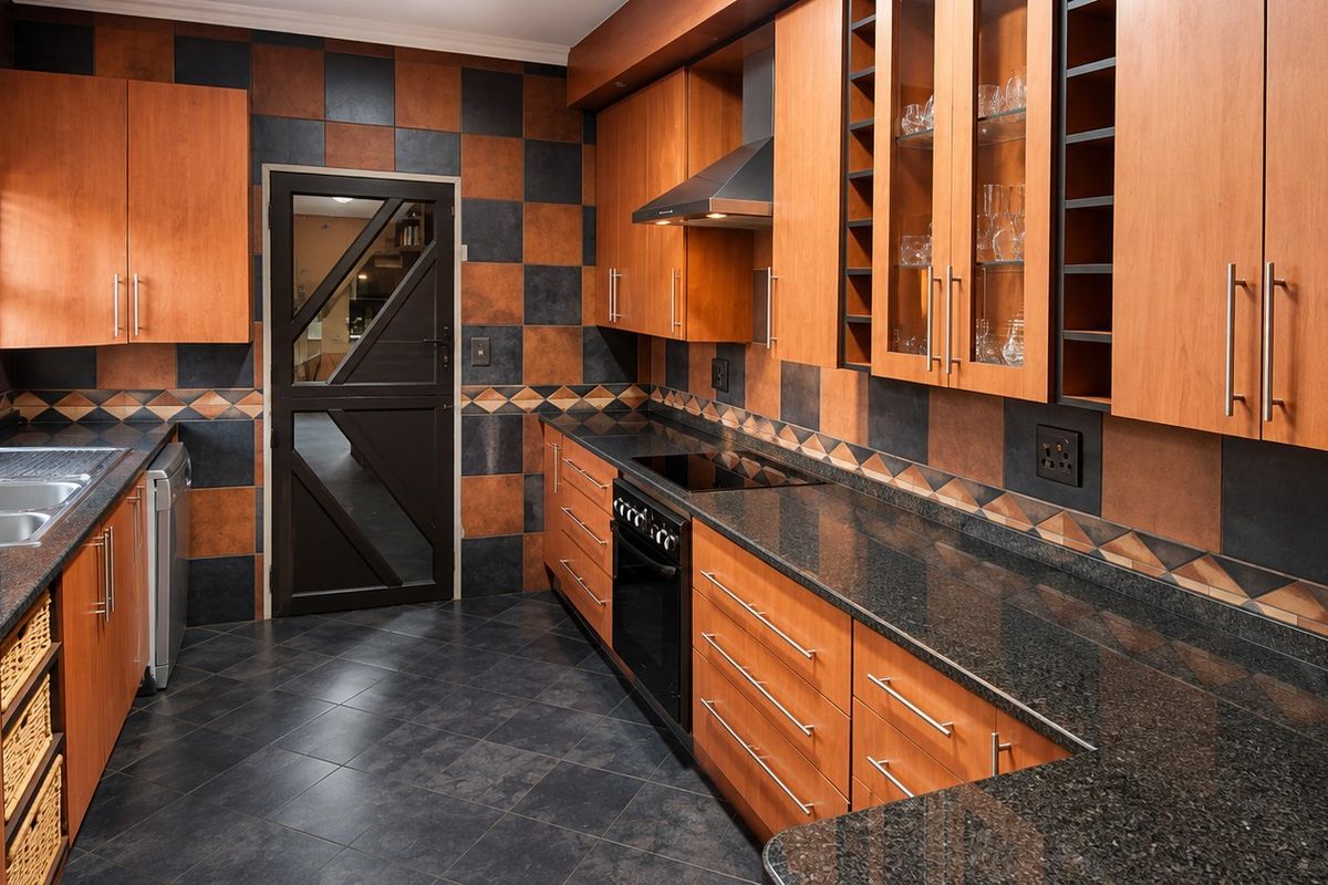 A functional kitchen featuring granite countertops, wooden cabinetry, built-in oven with hob, and a distinctive checkered tile splashback.