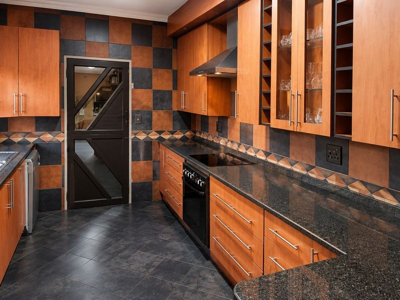 A functional kitchen featuring granite countertops, wooden cabinetry, built-in oven with hob, and a distinctive checkered tile splashback.