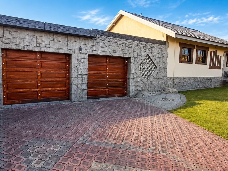 Front view of the property featuring a double garage with wooden doors, stone cladding facade, paved driveway, and a well-maintained lawn.