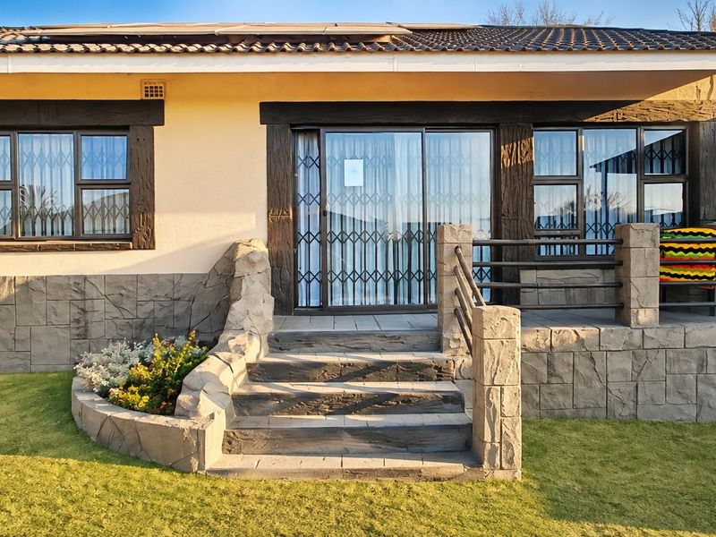 Front elevation of a house featuring stone cladding, a tiled roof with solar panels, security gates, and a raised entrance patio with concrete steps.