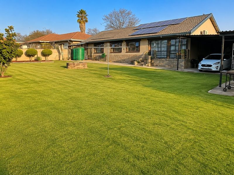 Spacious rear garden featuring a well-maintained lawn, covered patio area, solar panels on the roof, and secure perimeter fencing.
