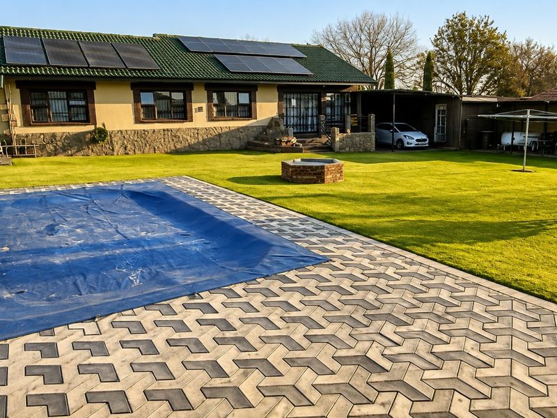 Spacious rear garden featuring a paved patio, swimming pool with cover, solar panels on the roof, and a convenient carport.