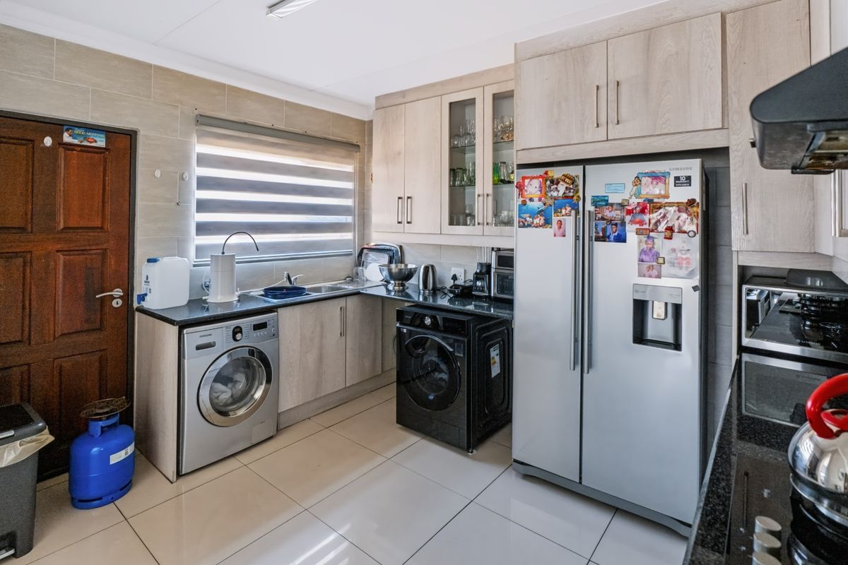 A functional kitchen featuring light wood-finish cabinetry, granite countertops, tiled flooring, and integrated space for laundry appliances.