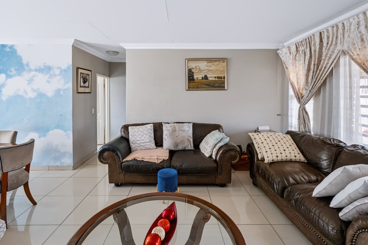 A well-lit living room featuring neutral tiled flooring, cove cornicing, and a feature wall with a sky-themed mural.