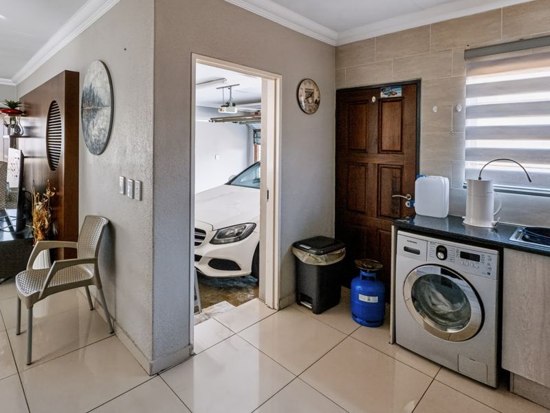 A functional laundry area featuring tiled flooring, built-in cabinetry with granite countertops, a sink, and direct access to the garage.