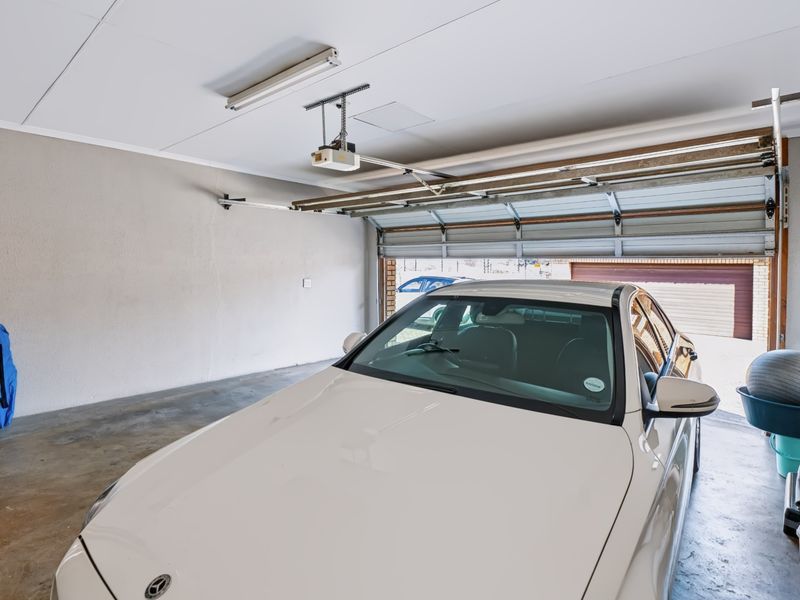 A functional single-car garage featuring concrete flooring, an automated door motor, and overhead fluorescent lighting.