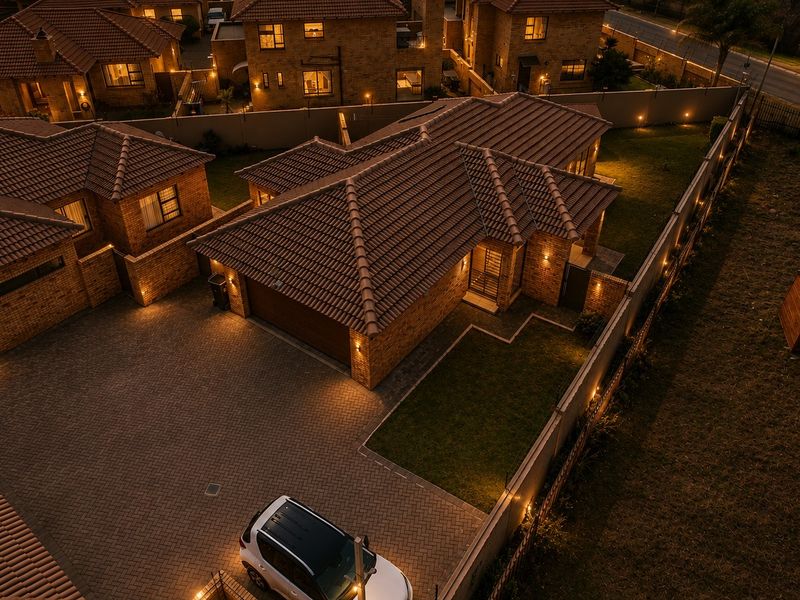 An elevated aerial view of a townhouse complex at night, showcasing the brick architecture, tiled roofs, paved driveways, and landscaped garden areas.