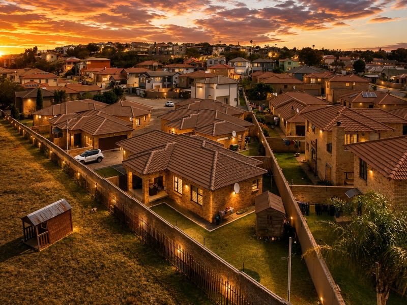 Aerial view of a residential townhouse complex at sunset, showcasing the property layout, tiled roofs, and surrounding neighborhood infrastructure.