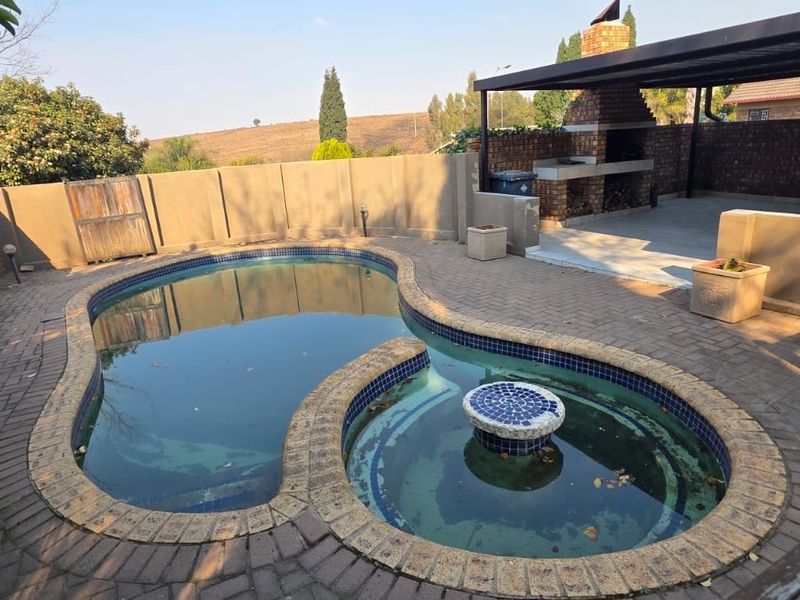 Outdoor entertainment area featuring a swimming pool with a built-in braai and covered patio space, requiring maintenance to restore its appeal.