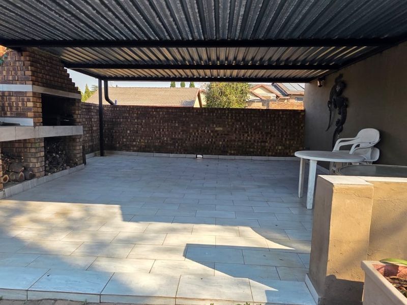 Covered outdoor patio area featuring a built-in brick braai, tiled flooring, and a corrugated metal roof, ideal for outdoor entertaining.