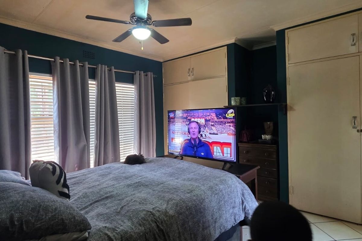 A bedroom featuring built-in cupboards, tiled flooring, and a ceiling fan, offering a functional space with potential for cosmetic updates.