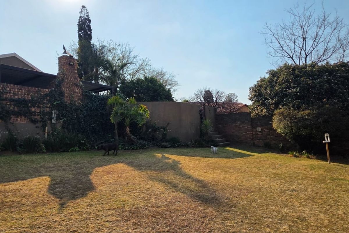 Spacious rear garden featuring a brick chimney, covered patio area, and stone stairs leading to a raised section of the yard.